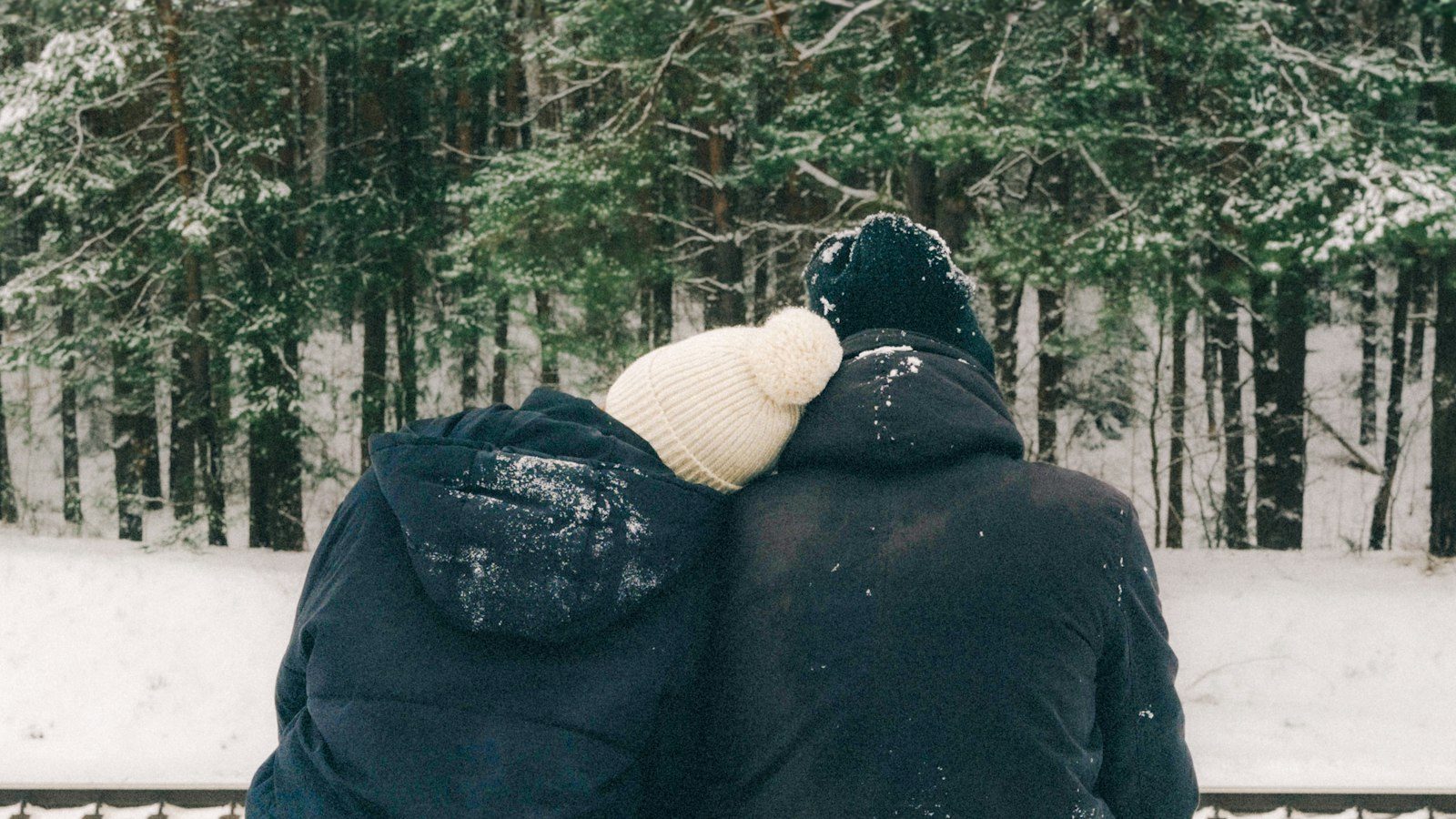 雪景色の中でお揃いの黒いアウターを着て並ぶカップルの後ろ姿
